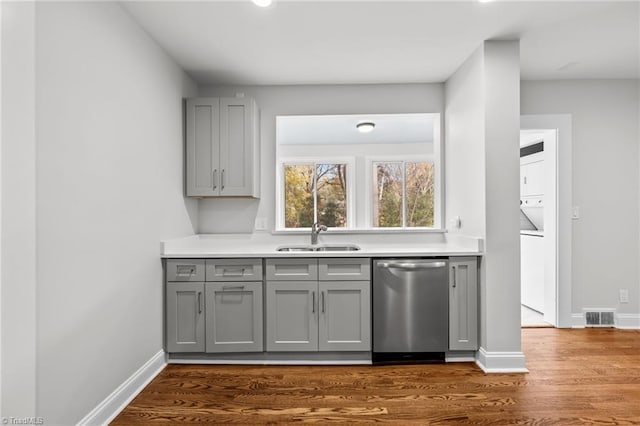 kitchen featuring dishwasher, dark hardwood / wood-style flooring, stacked washer and dryer, and sink