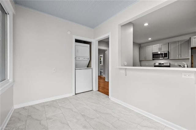 kitchen with gray cabinetry, stacked washer / drying machine, sink, and stainless steel appliances