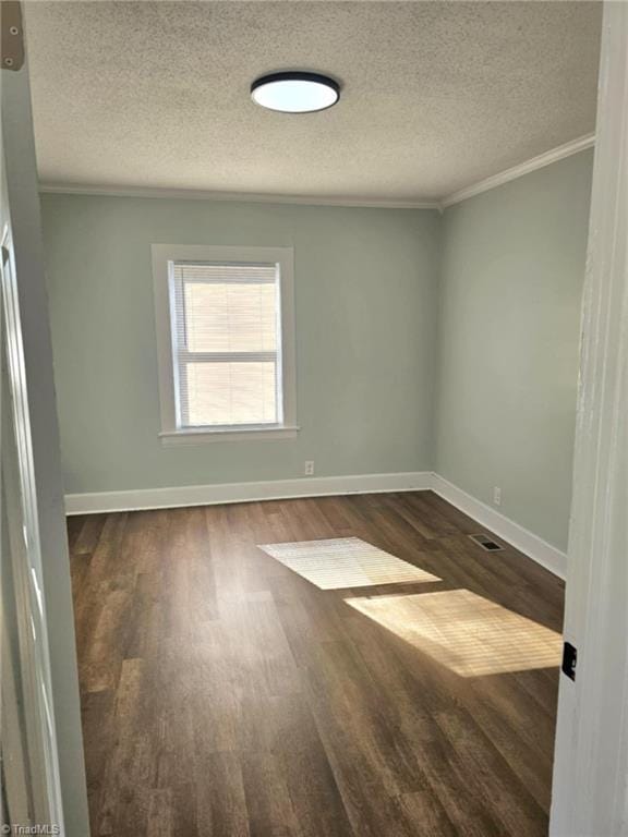 empty room featuring baseboards, dark wood finished floors, visible vents, and crown molding