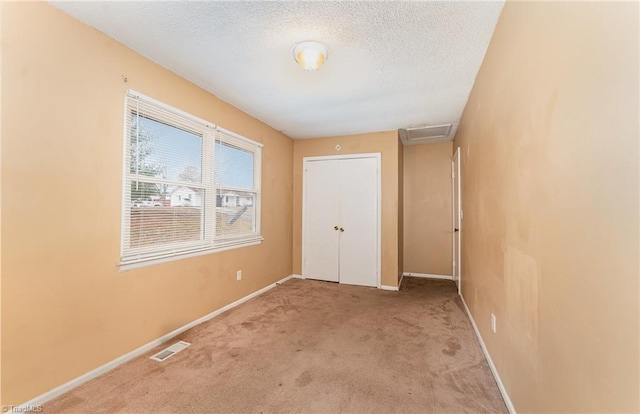 unfurnished bedroom with visible vents, a textured ceiling, carpet, baseboards, and attic access