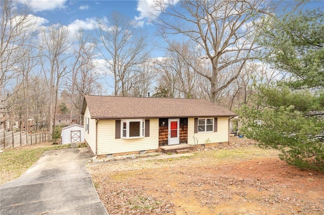 view of front of property featuring an outbuilding, fence, a shingled roof, concrete driveway, and crawl space