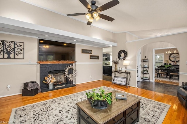 living room featuring a fireplace, wood-type flooring, and ceiling fan with notable chandelier