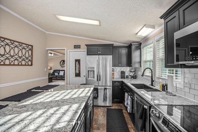 kitchen with backsplash, light stone counters, stainless steel appliances, vaulted ceiling, and sink