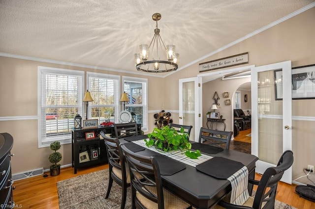 dining room featuring vaulted ceiling, light hardwood / wood-style flooring, ornamental molding, a textured ceiling, and a chandelier