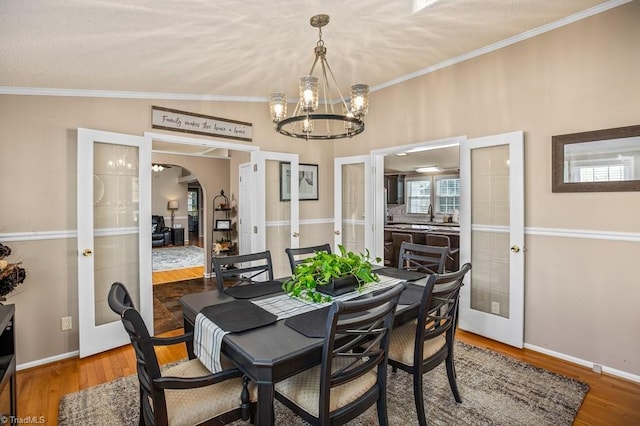 dining space featuring lofted ceiling, an inviting chandelier, french doors, ornamental molding, and wood-type flooring