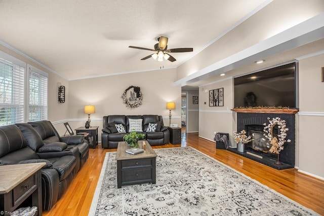 living room with a fireplace, light hardwood / wood-style floors, ceiling fan, and ornamental molding