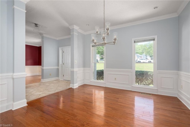 unfurnished dining area featuring an inviting chandelier, a textured ceiling, wood finished floors, and wainscoting