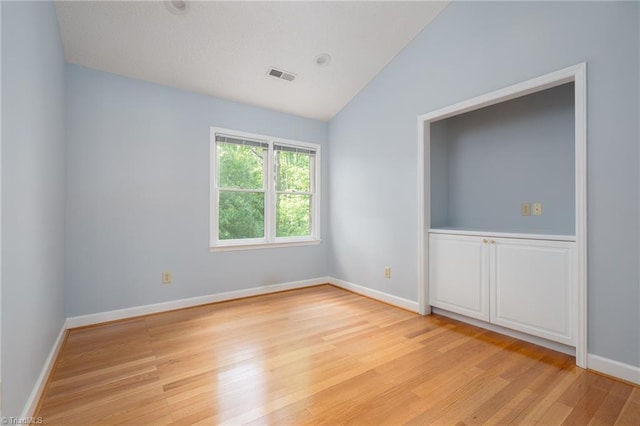spare room with visible vents, baseboards, vaulted ceiling, and light wood-type flooring
