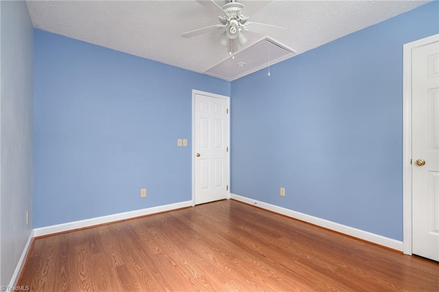 spare room featuring attic access, ceiling fan, wood finished floors, and baseboards