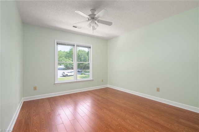 spare room featuring a ceiling fan, visible vents, baseboards, a textured ceiling, and wood finished floors
