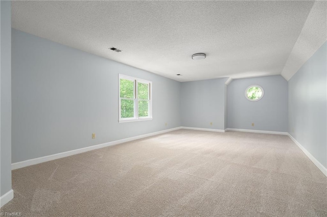 carpeted spare room featuring baseboards, visible vents, a textured ceiling, and lofted ceiling
