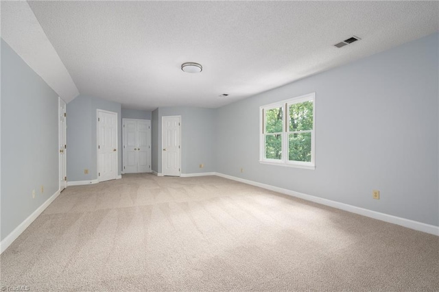 empty room with light colored carpet, visible vents, a textured ceiling, and baseboards