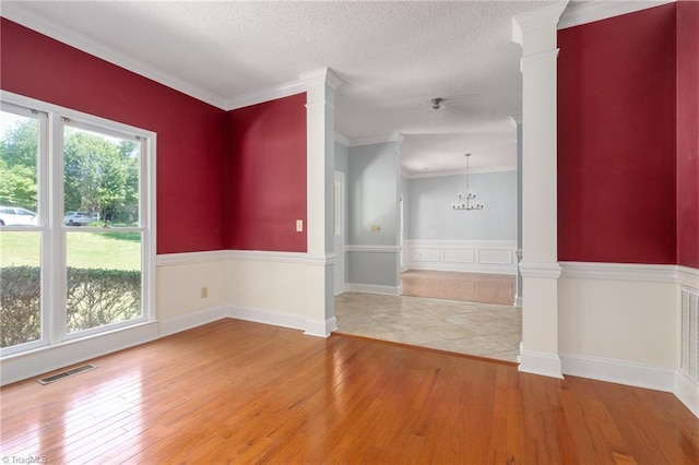 empty room featuring ornate columns, visible vents, crown molding, and light wood-style flooring
