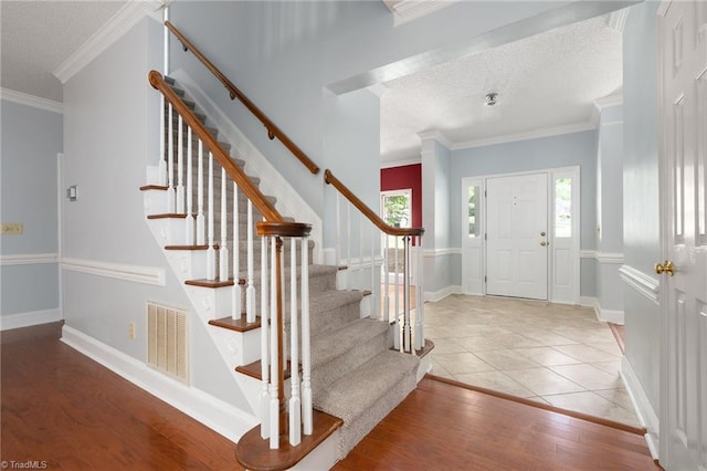 staircase featuring crown molding, visible vents, baseboards, a textured ceiling, and wood finished floors