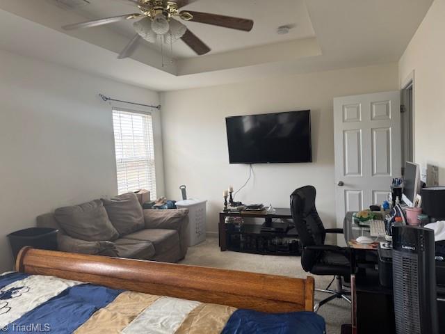 carpeted bedroom featuring ceiling fan and a raised ceiling