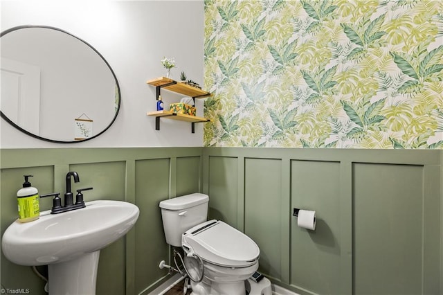 bathroom with a sink, a decorative wall, toilet, and a wainscoted wall