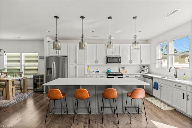 kitchen with a kitchen island, beverage cooler, a kitchen bar, white cabinets, and stainless steel appliances