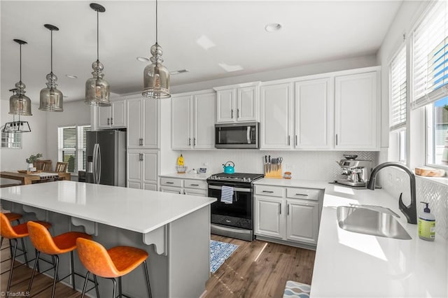 kitchen with decorative backsplash, a kitchen island, light countertops, a sink, and stainless steel appliances