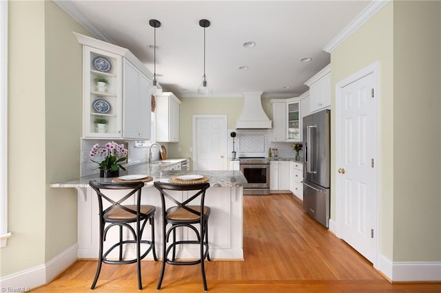 kitchen featuring light stone countertops, premium range hood, ornamental molding, appliances with stainless steel finishes, and a peninsula