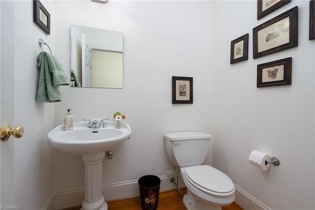 half bathroom featuring a sink, baseboards, toilet, and wood finished floors