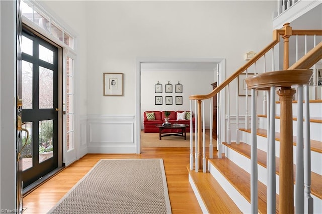 entryway featuring light wood finished floors, stairway, wainscoting, a decorative wall, and a towering ceiling