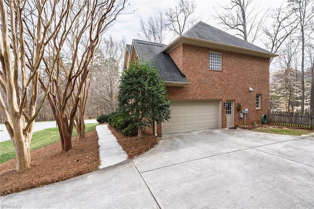 view of side of home with fence, roof with shingles, concrete driveway, a garage, and brick siding