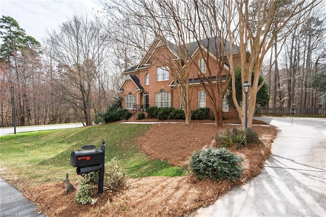 traditional-style house featuring brick siding, a front lawn, and fence