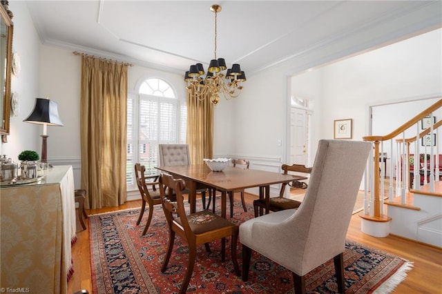 dining space featuring stairs, light wood-type flooring, a notable chandelier, and crown molding