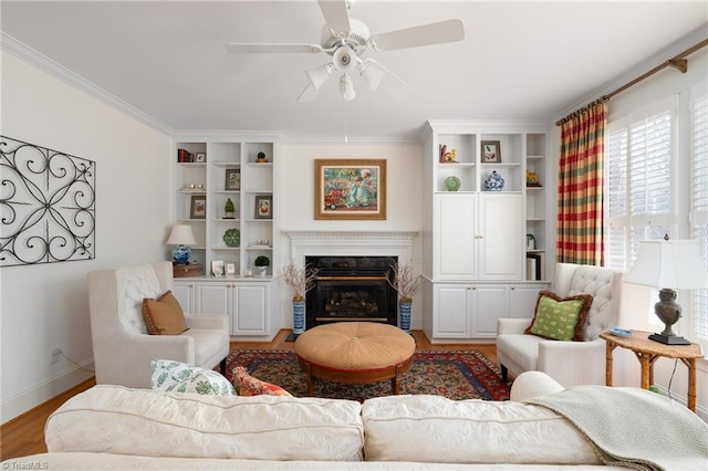 living room with ornamental molding, a ceiling fan, a glass covered fireplace, wood finished floors, and baseboards