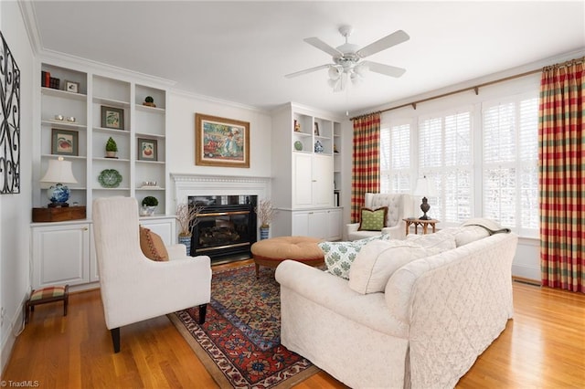 living room featuring a glass covered fireplace, crown molding, light wood-type flooring, and ceiling fan