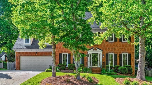 colonial-style house with brick siding, an attached garage, driveway, and fence