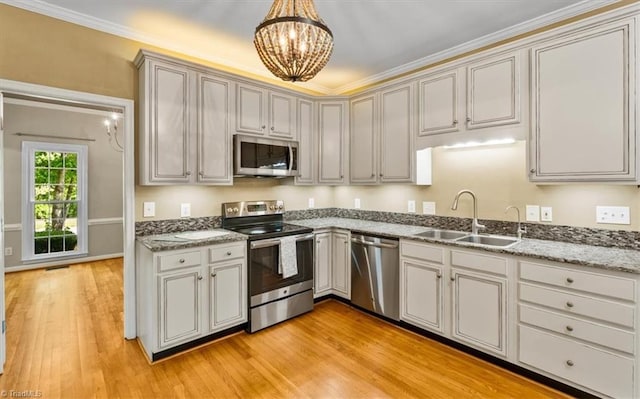 kitchen with a notable chandelier, appliances with stainless steel finishes, a sink, light wood finished floors, and decorative light fixtures