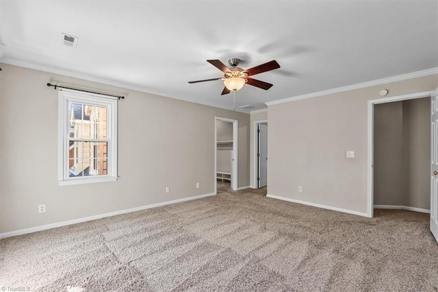 unfurnished bedroom featuring carpet floors, baseboards, ornamental molding, and a walk in closet