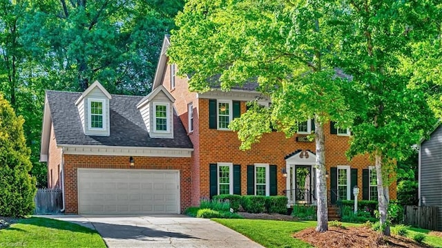 colonial house featuring fence, roof with shingles, brick siding, an attached garage, and driveway