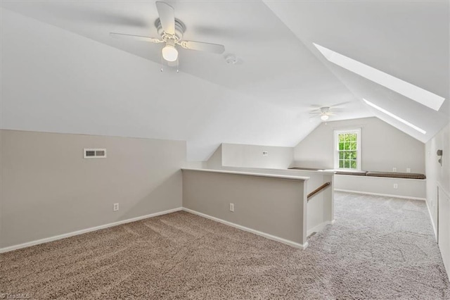 additional living space featuring a ceiling fan, visible vents, lofted ceiling with skylight, and carpet