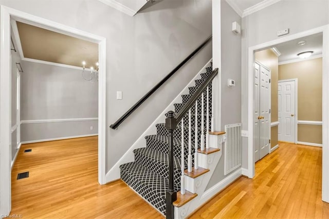 stairway with baseboards, visible vents, ornamental molding, and wood finished floors