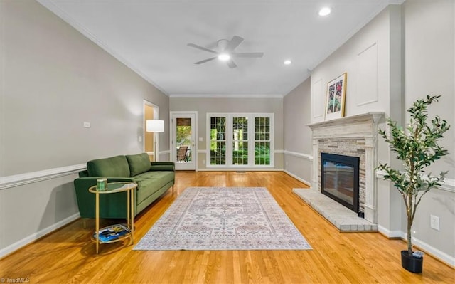living room with crown molding, ceiling fan, a glass covered fireplace, baseboards, and wood finished floors