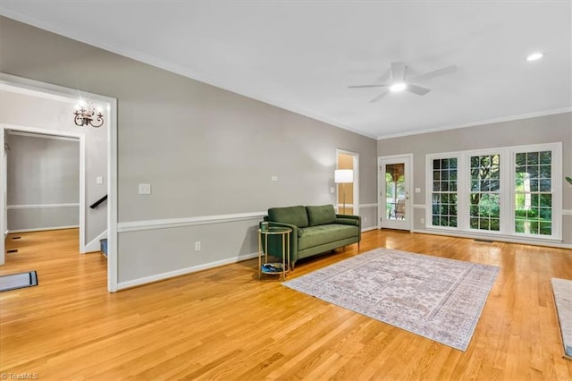living area featuring crown molding, baseboards, ceiling fan with notable chandelier, and wood finished floors