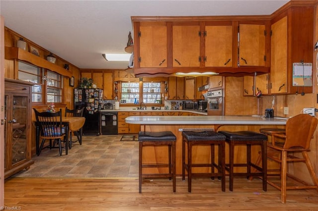 kitchen with black appliances, kitchen peninsula, light hardwood / wood-style floors, and a breakfast bar