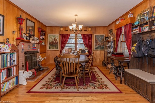 dining space featuring a brick fireplace, light wood-type flooring, wood walls, and an inviting chandelier