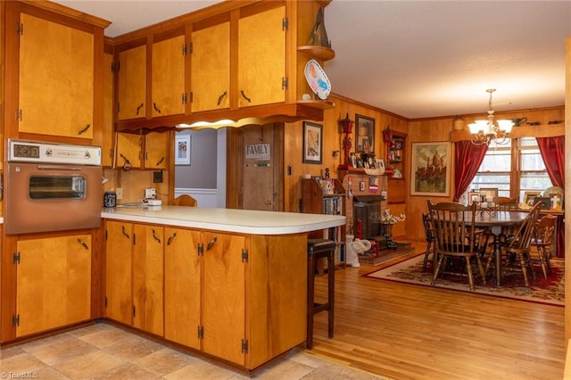 kitchen with kitchen peninsula, a notable chandelier, oven, ornamental molding, and light wood-type flooring