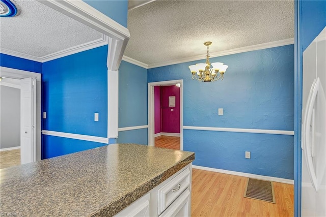 kitchen featuring light hardwood / wood-style flooring, ornamental molding, white cabinets, white fridge, and a textured ceiling