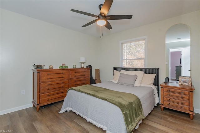 bedroom with a ceiling fan, wood finished floors, arched walkways, and baseboards