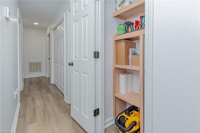 corridor featuring baseboards, visible vents, and light wood finished floors