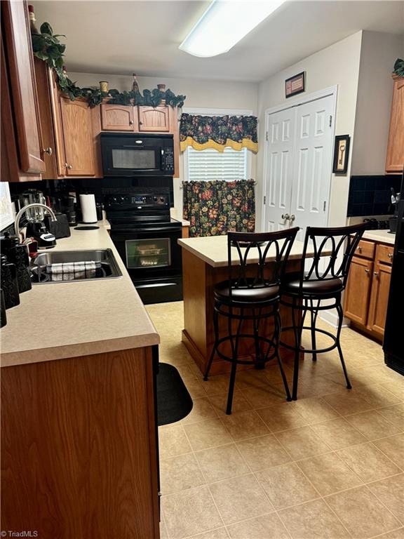 kitchen with sink, a kitchen bar, decorative backsplash, a kitchen island, and black appliances