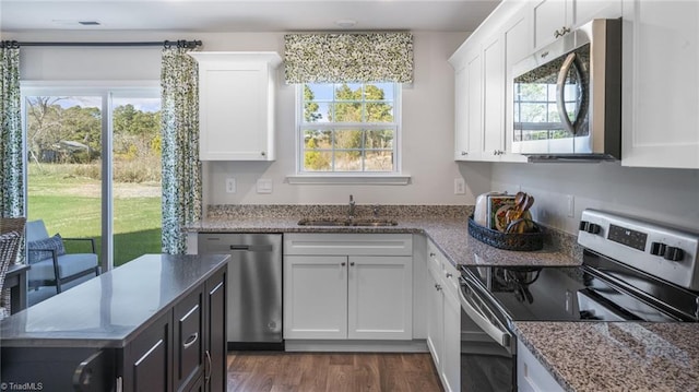 kitchen with light stone counters, dark wood-style flooring, a sink, white cabinetry, and appliances with stainless steel finishes