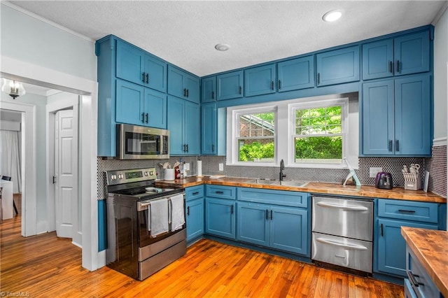 kitchen with appliances with stainless steel finishes, wooden counters, blue cabinets, a sink, and ornamental molding