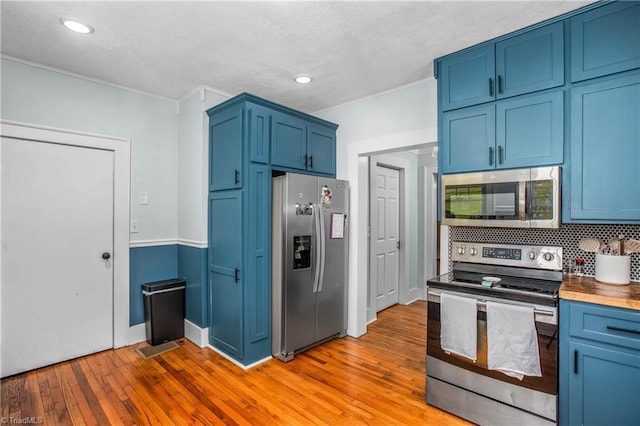 kitchen with appliances with stainless steel finishes, blue cabinetry, light wood-style flooring, ornamental molding, and backsplash