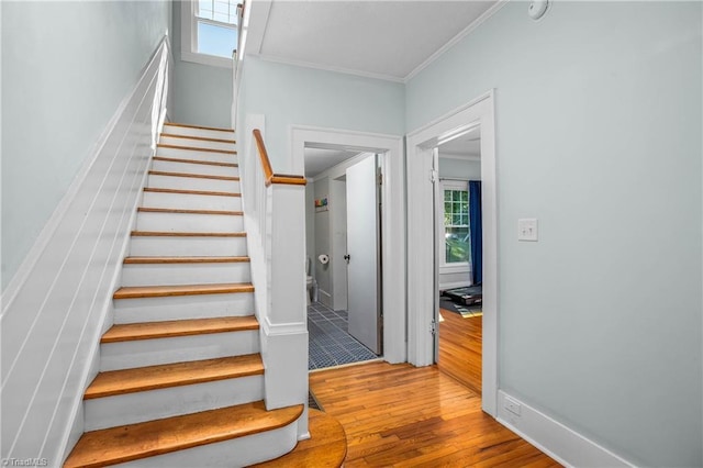 stairway featuring wood finished floors, ornamental molding, and baseboards