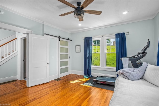 sitting room featuring light wood-style floors, crown molding, a barn door, a ceiling fan, and baseboards